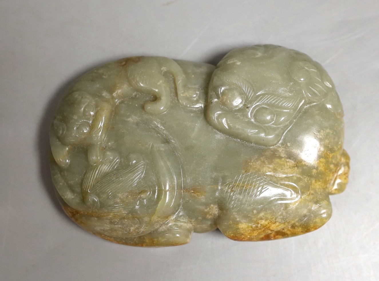 A Chinese celadon and a russet jade ‘lion dog and cub’ plaque, 11.5cm across
